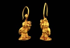 A Pair of gold earrings in the form of a boy holding lotus fronds by 
